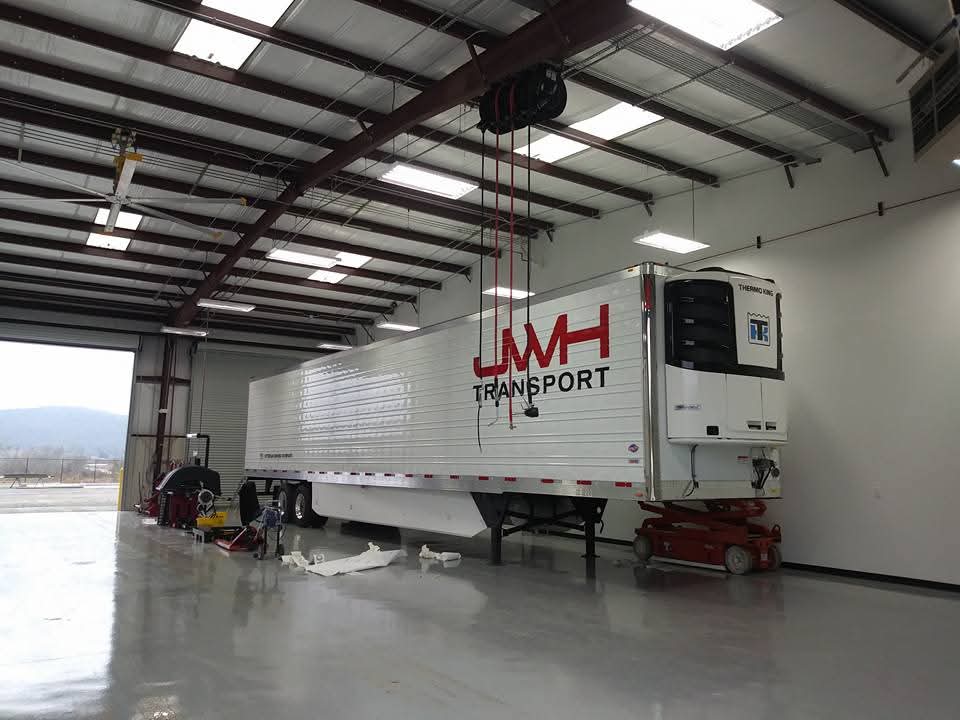 White reefer trailer with red JWH Transport cut vinyl lettering in an install bay