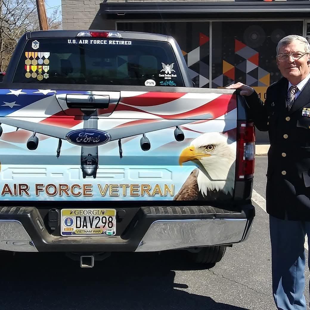 Ford F-150 tailgate wrapped with an American flag and bald eagle Air Force veteran design, owner standing beside it in dress uniform